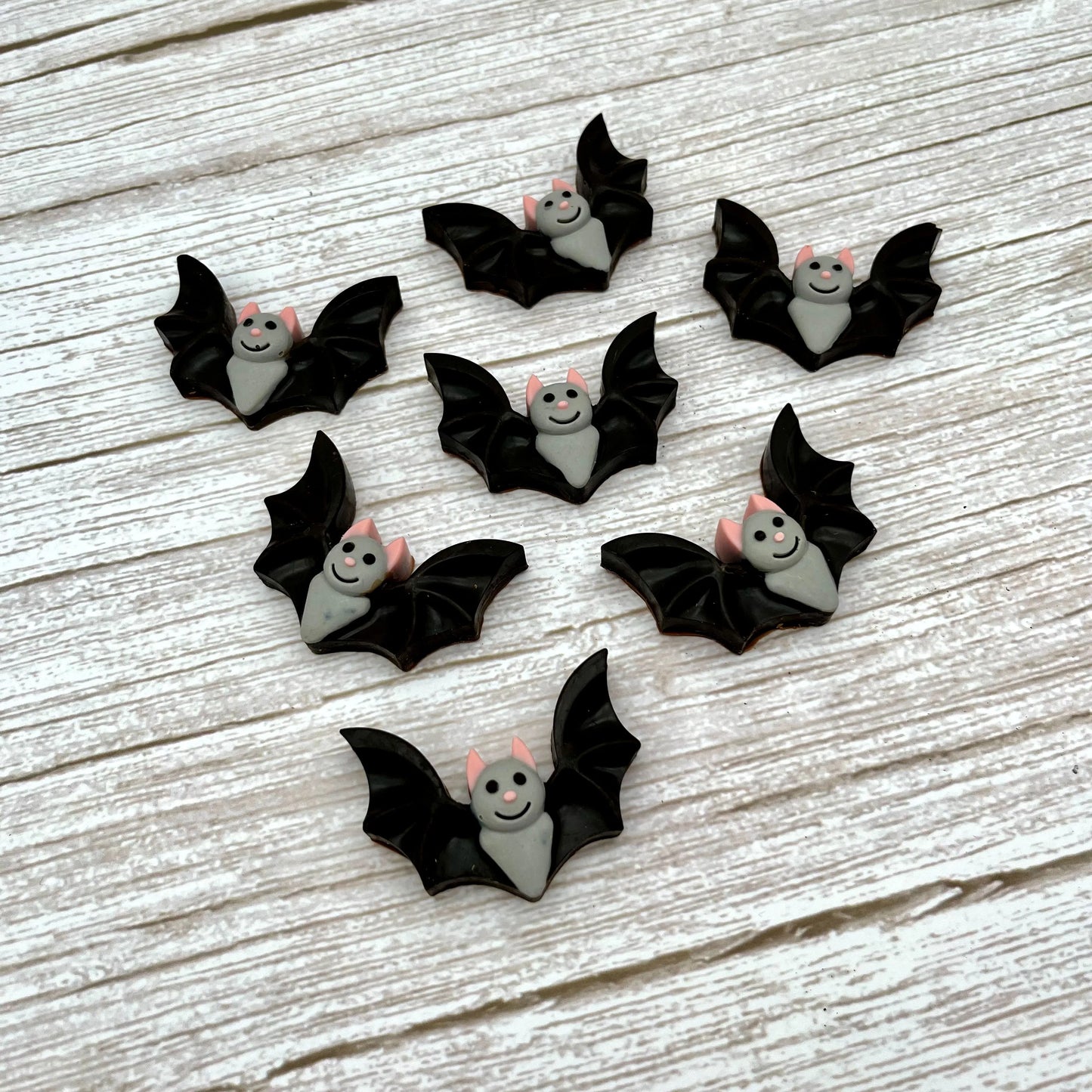 Black and grey bat-shaped chocolates with pink ears and noses and big smile. Displayed on a wooden surface.