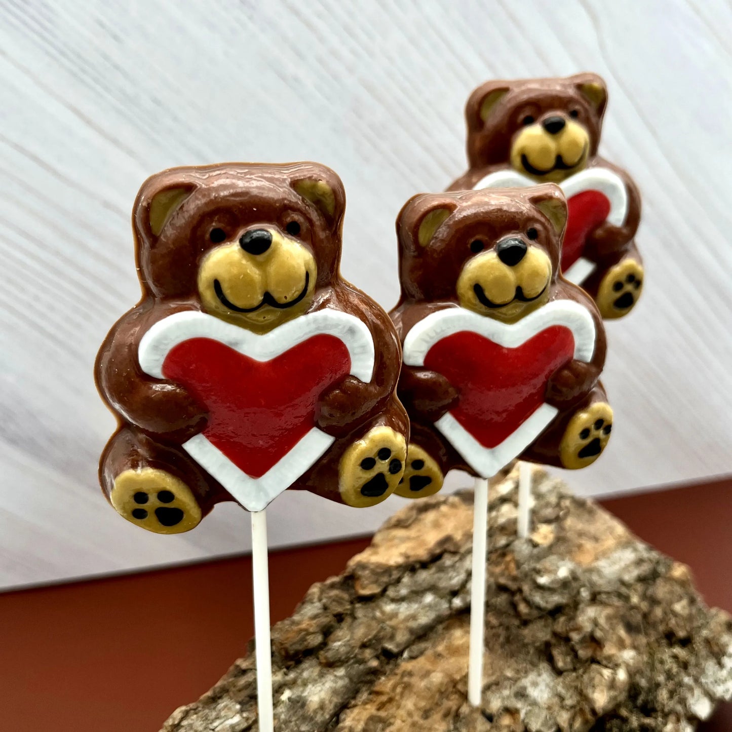 Three brown chocolate teddy bear suckers with big red hearts on a white background.
