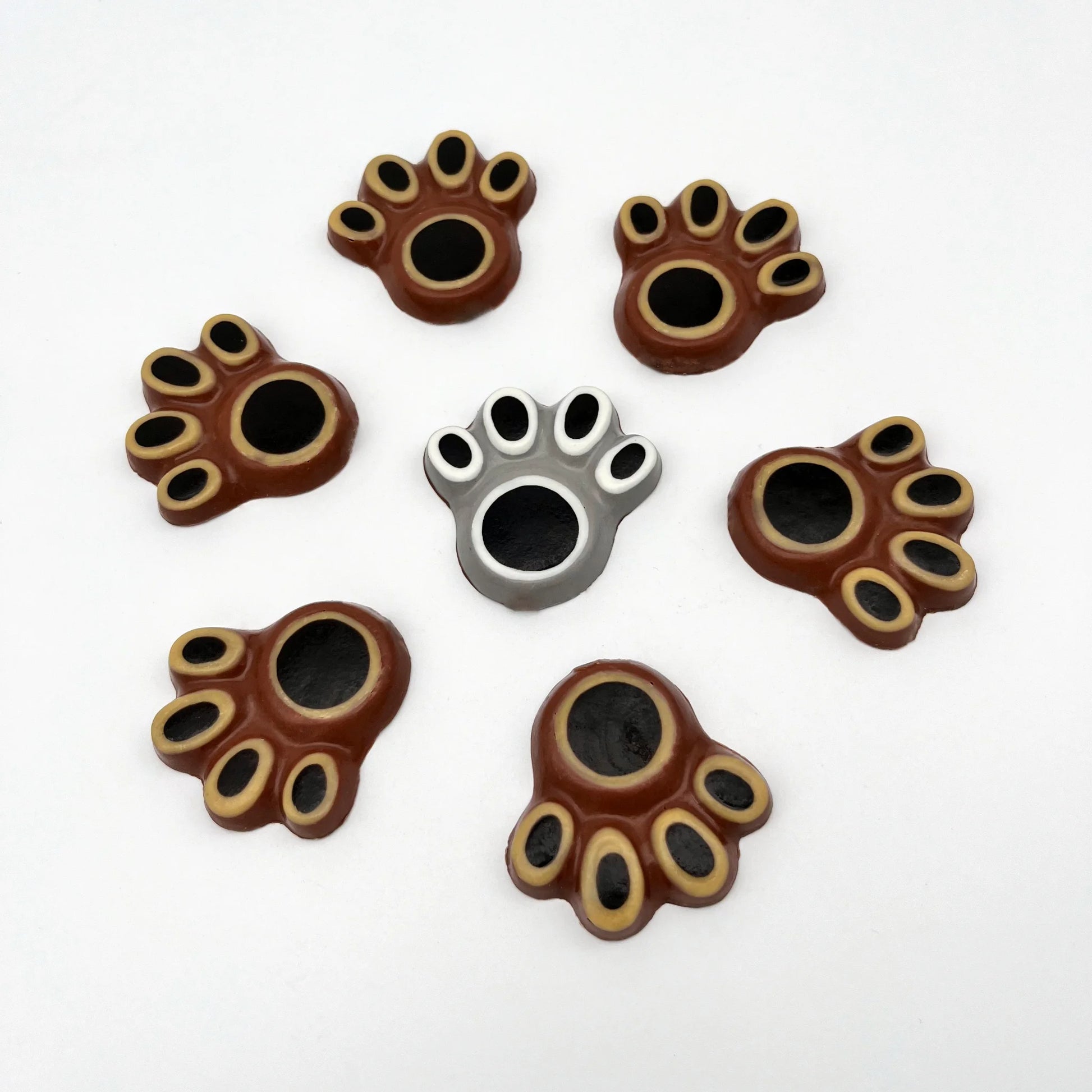 Selection of bear paw chocolates, hand-painted with black pads surrounded by white or beige, with grey or brown background.