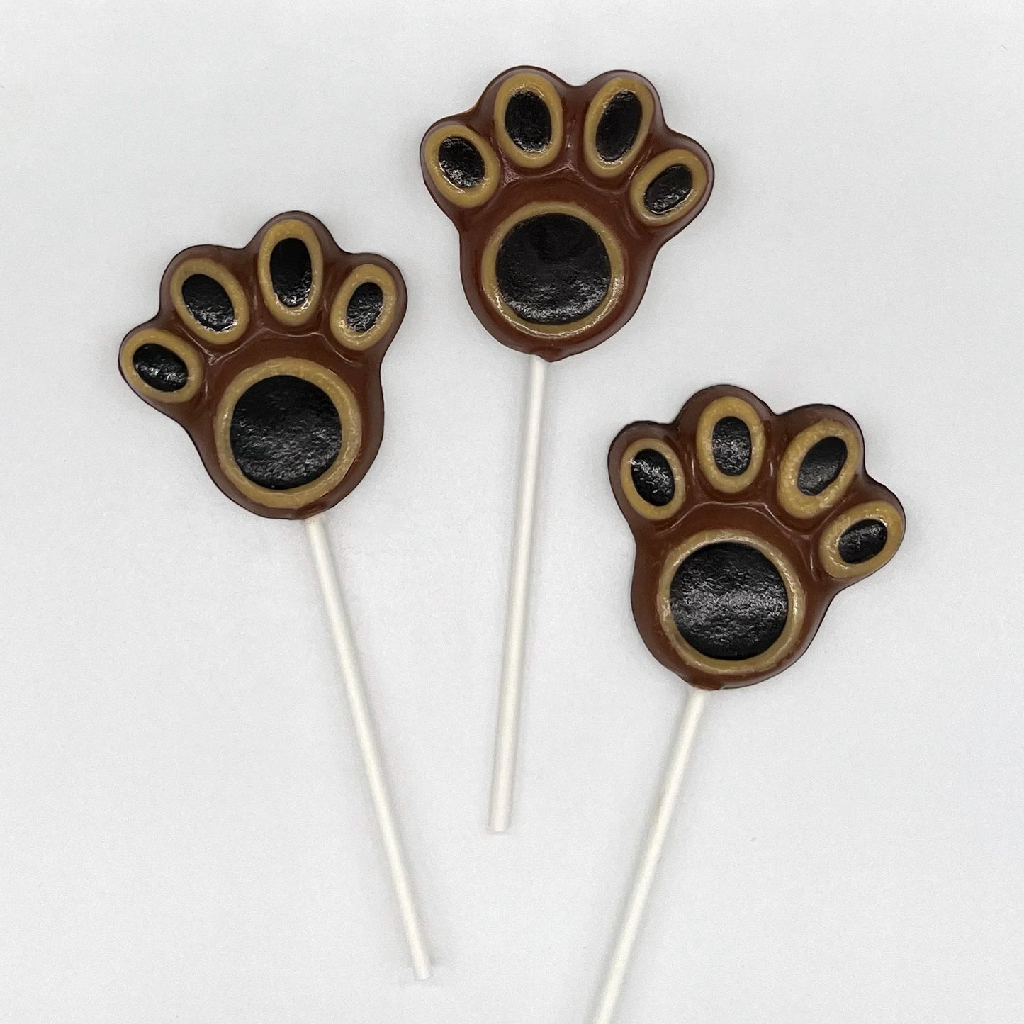 Bear paw chocolates, hand-painted with black pads, surrounded by beige, with a dark brown background.