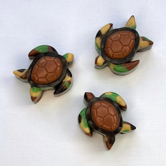 Chocolate turtles that look like they are swimming, coloured in a camouflage pattern with a brown and black shell.