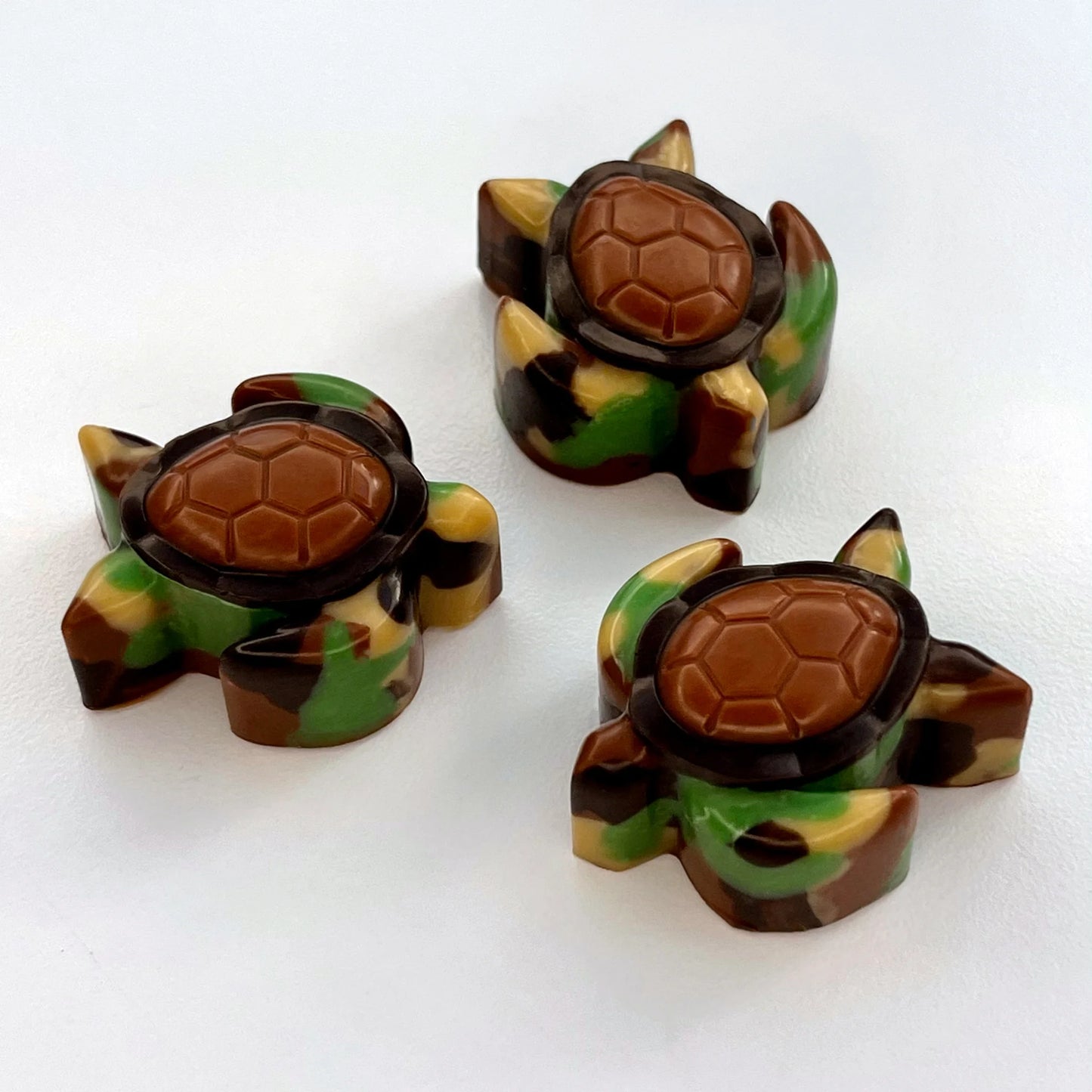 Chocolate turtles that look like they are swimming, coloured in a camouflage pattern with a brown and black shell.