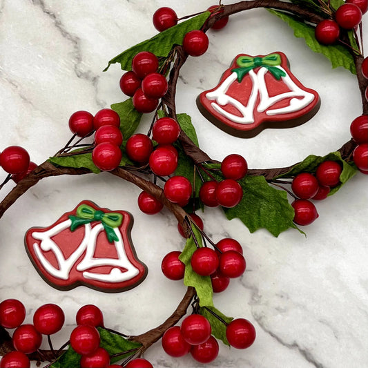 Red, and white chocolate Christmas bells with green bows. Surrounded by holly decorations on a marble surface.