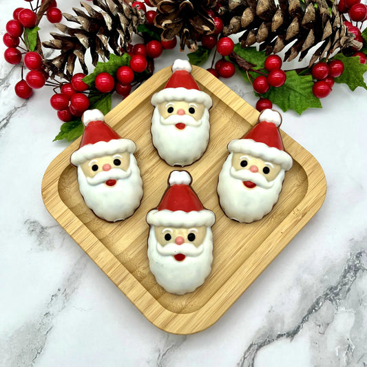 Four Santa Claus chocolates on a wooden tray, with Christmas decorations and a marble background.