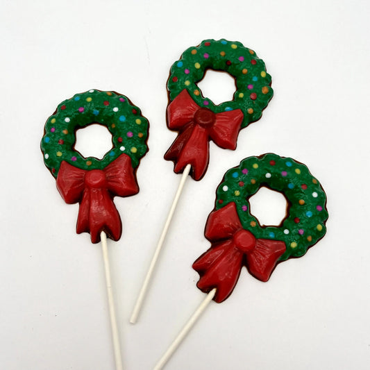 Three chocolate Christmas wreath suckers with red bows and multi-colour "lights", set against a white background.