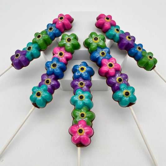 Chocolate forget-me-not flower suckers in vibrant blue, pink, green, purple, and turquoise, all with a black and yellow centre.