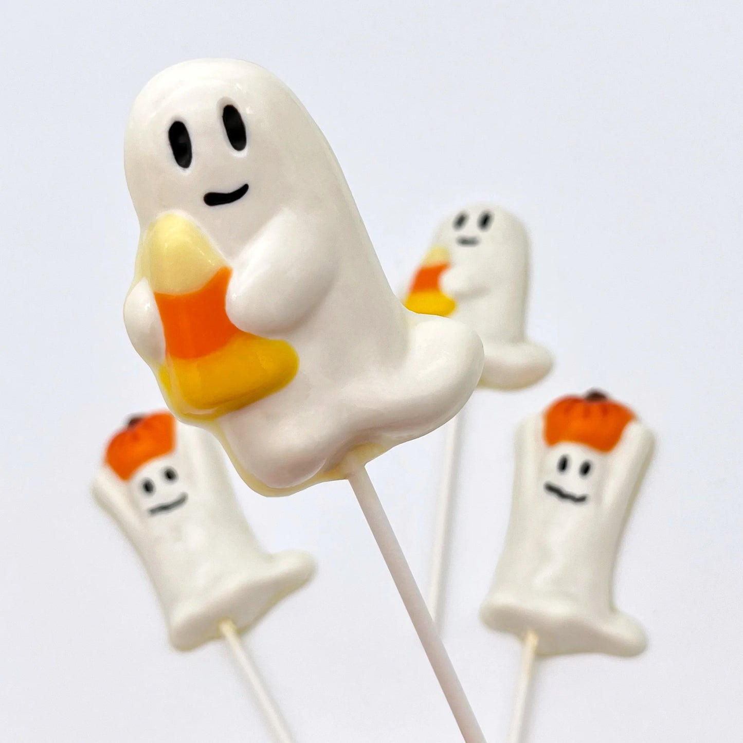 The cutest happy ghost with big black eyes and smile, holding a candy corn - all made from chocolate.