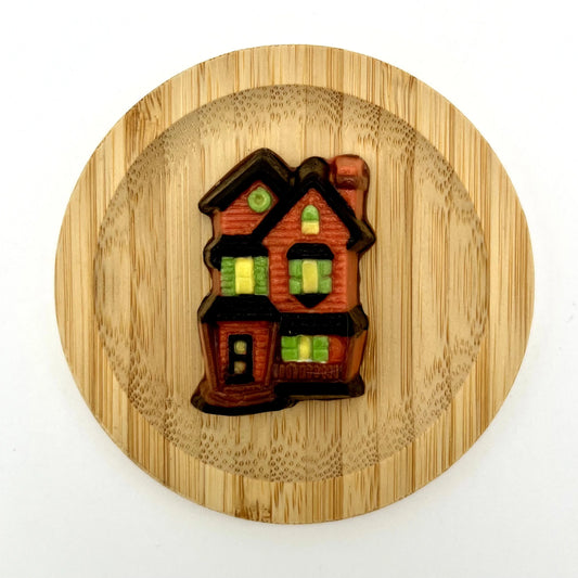 Chocolate haunted house hand-painted in brick red, with glowing yellow windows, green shutters and black roof.