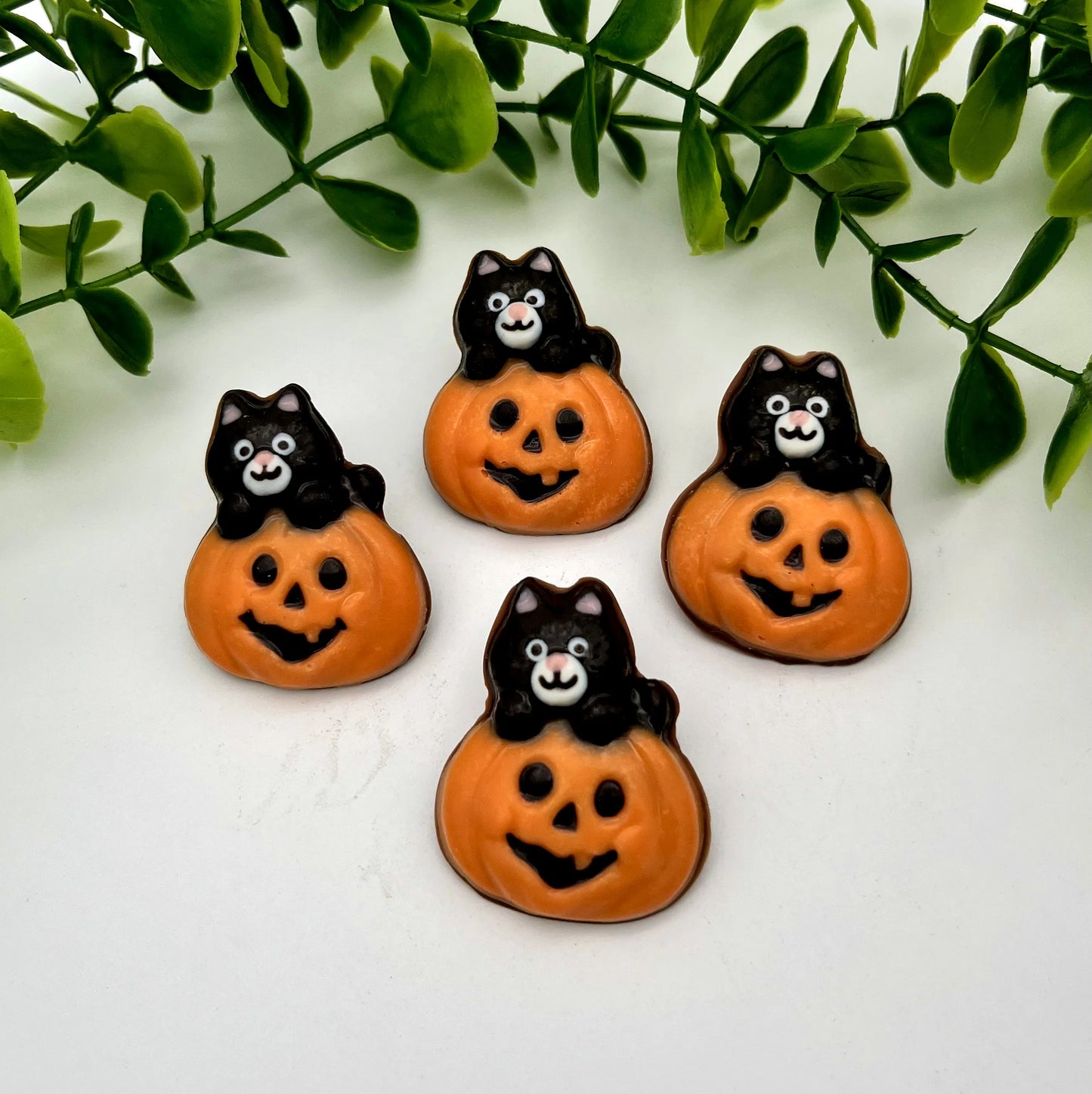 Four chocolates of orange pumpkins with carved faces with black and white cats on top.