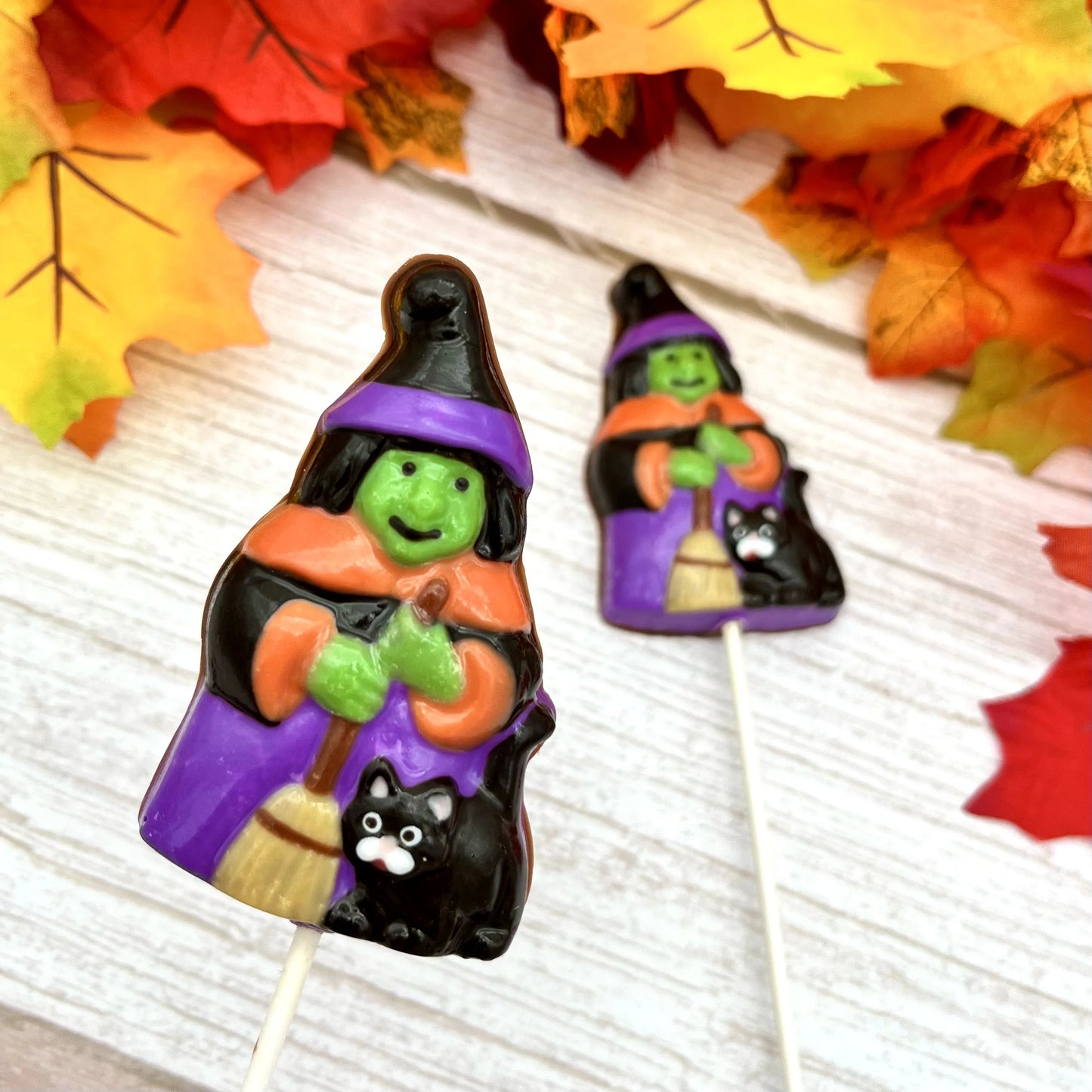 Halloween-themed chocolate suckers of witches in traditional costume of black hats, cape, broom and a black cat.