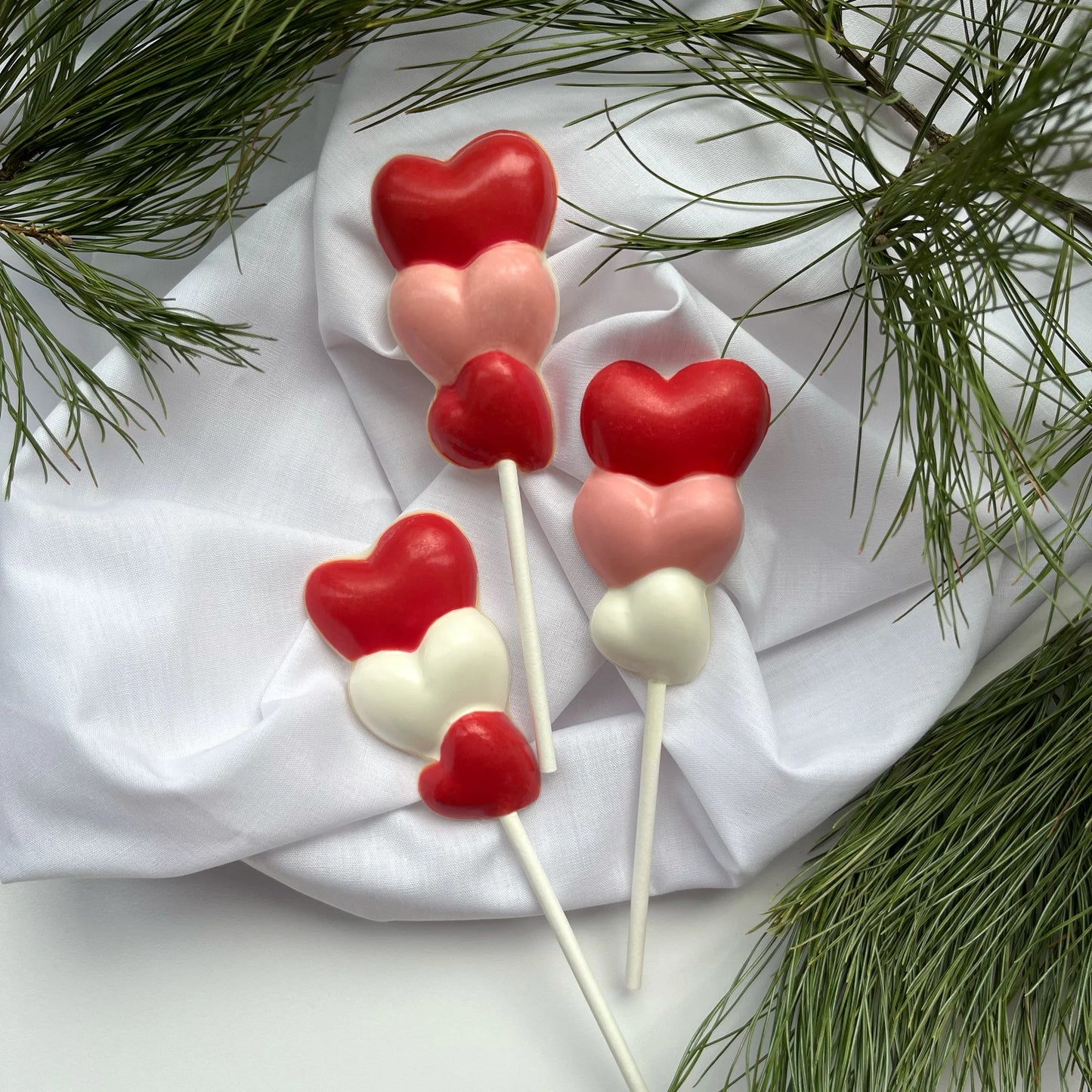 Three hearts stacked on top of each other, on a stick as a chocolate sucker. Variations of white, pink and red on each.
