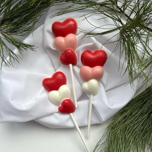 Three hearts stacked on top of each other, on a stick as a chocolate sucker. Variations of white, pink and red on each.