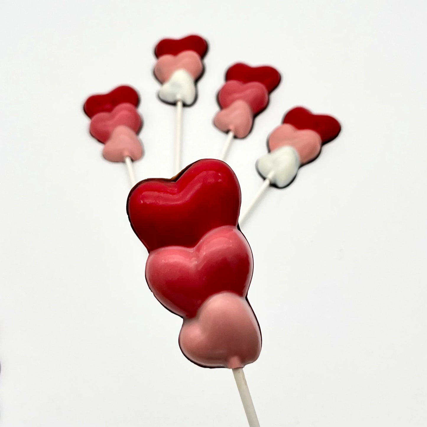 Three hearts stacked on top of each other, on a stick as a chocolate sucker. Variations of white, pink and red on each.