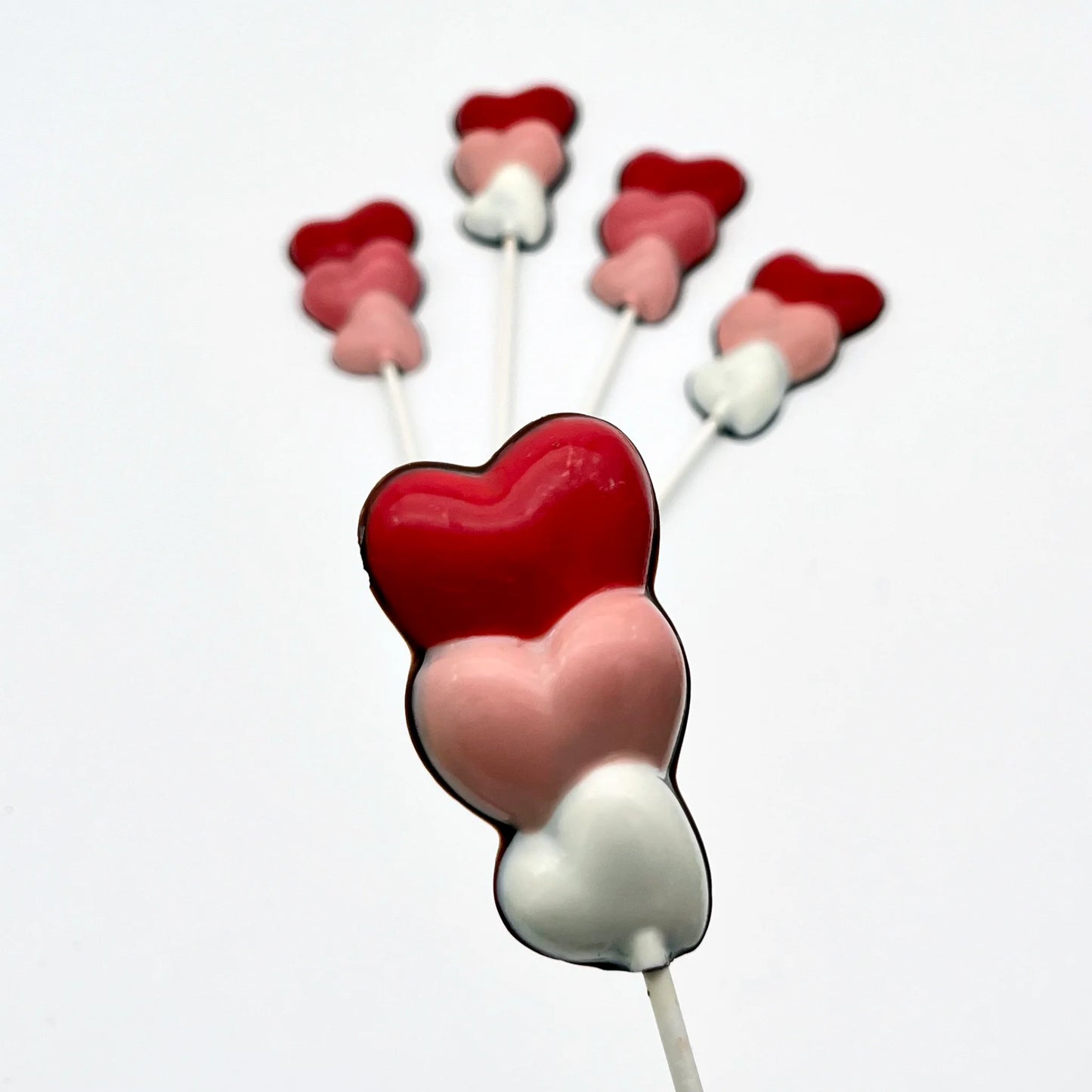 Three hearts stacked on top of each other, on a stick as a chocolate sucker. Variations of white, pink and red on each.