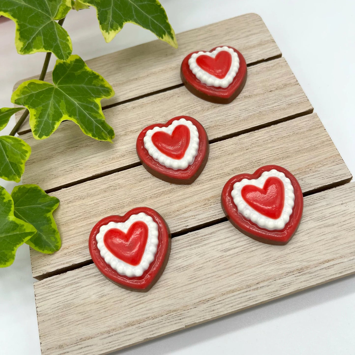 Heart-shaped chocolates on a wooden board, each with a red outer heart and a red heart centre surrounded by a white border.