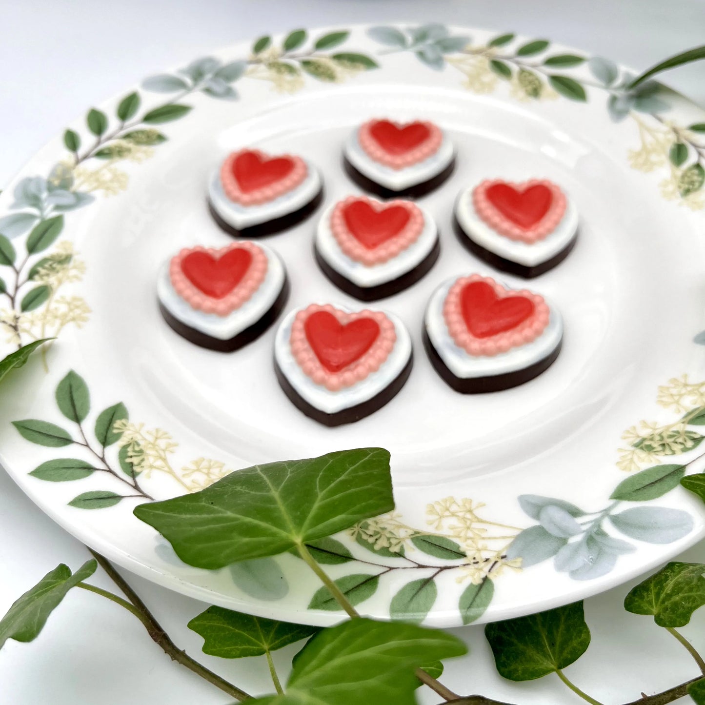 Heart-shaped chocolates on a wooden board, each with a white outer heart and a red heart centre surrounded by a pink border.
