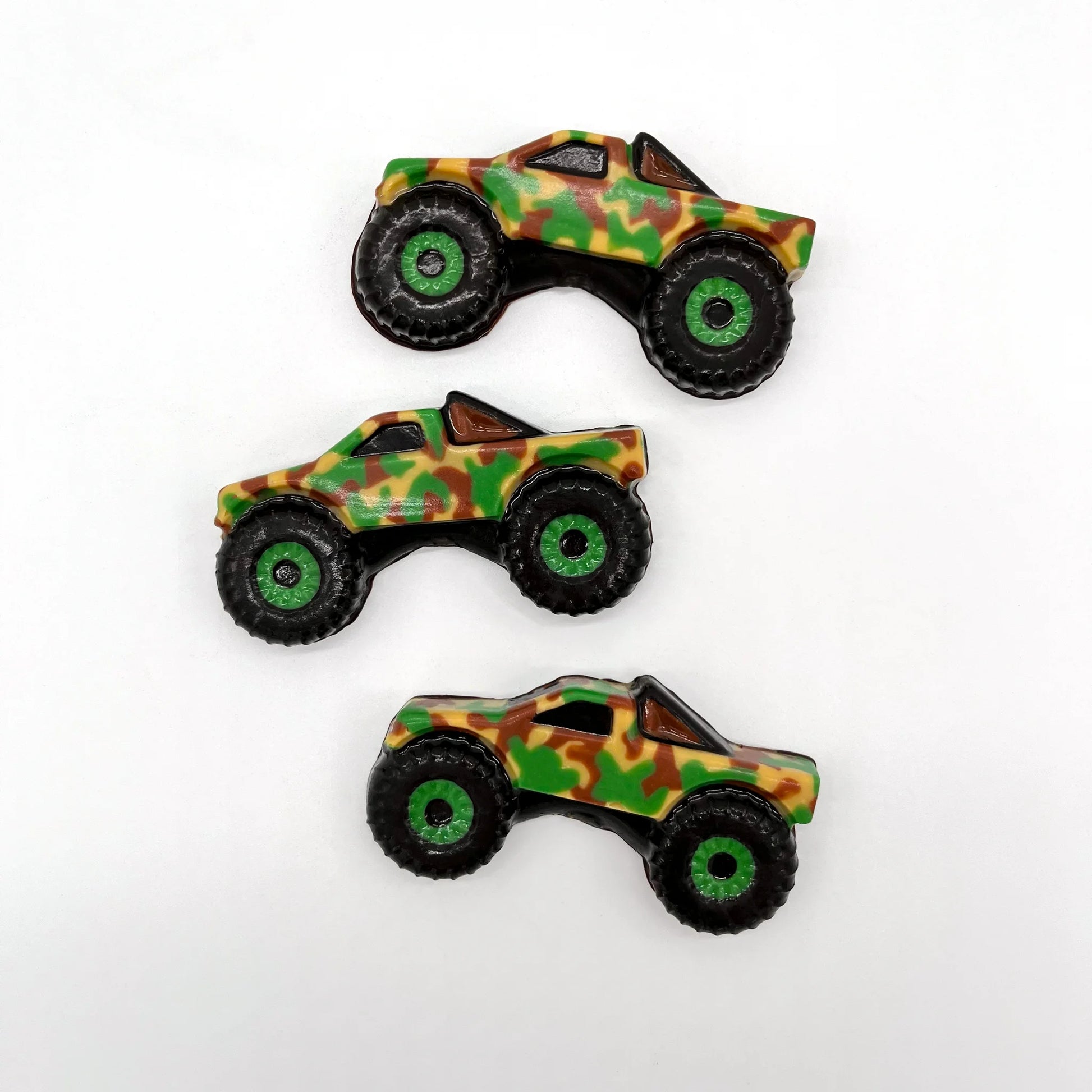 Three camo-patterned monster truck-shaped chocolates with green and black wheels and detailing.