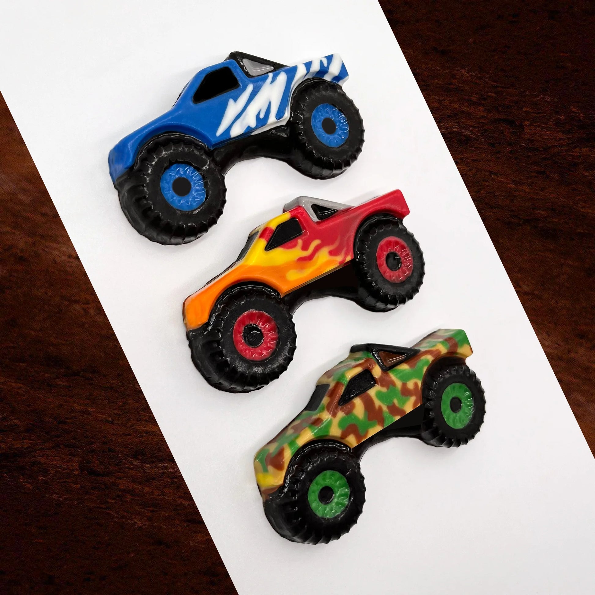 Three chocolates shaped like monster trucks in blue with white lightening, red with flames, and camouflage colours.