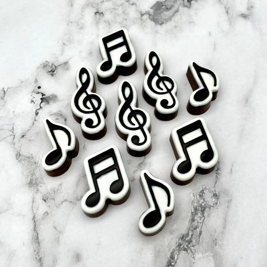 A selection of black and white chocolate music notes - treble clef, sixteen and eighth notes, all placed on a marble background.