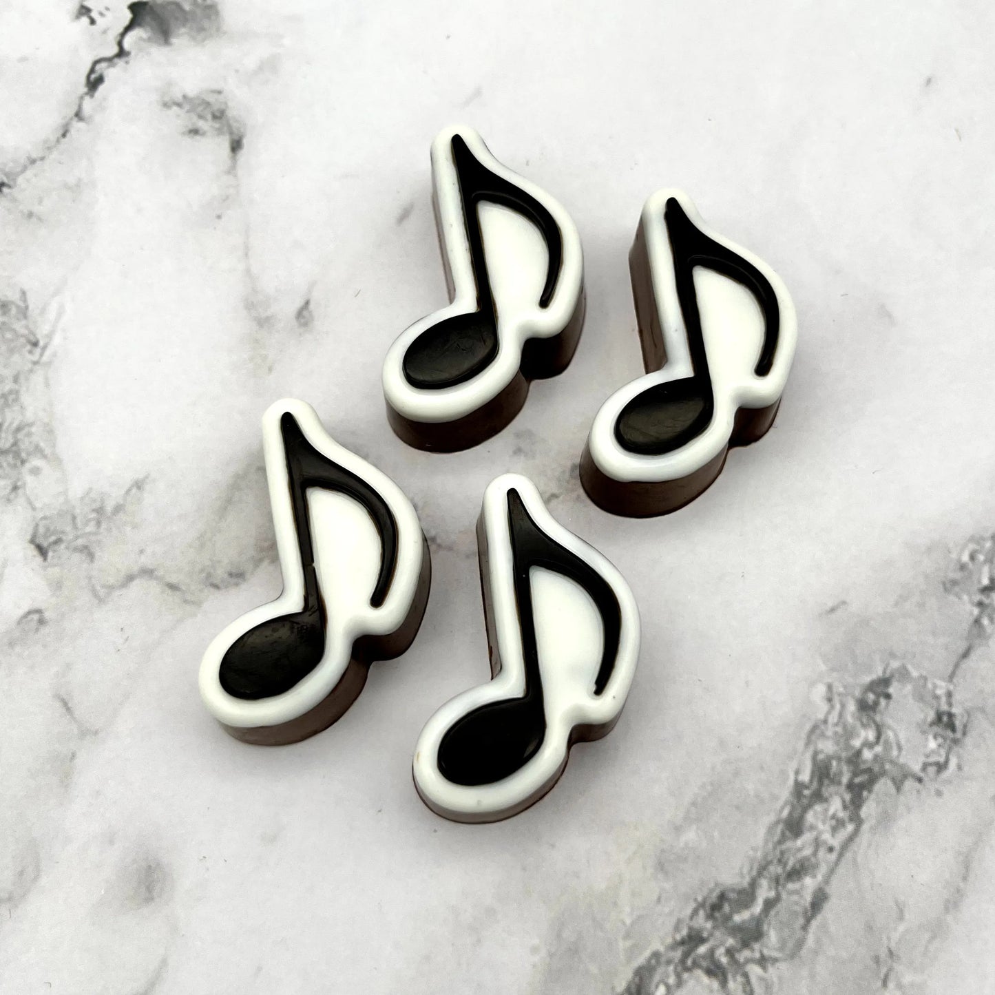 Black and white eighth music notes, made from chocolate, placed on a marble background.
