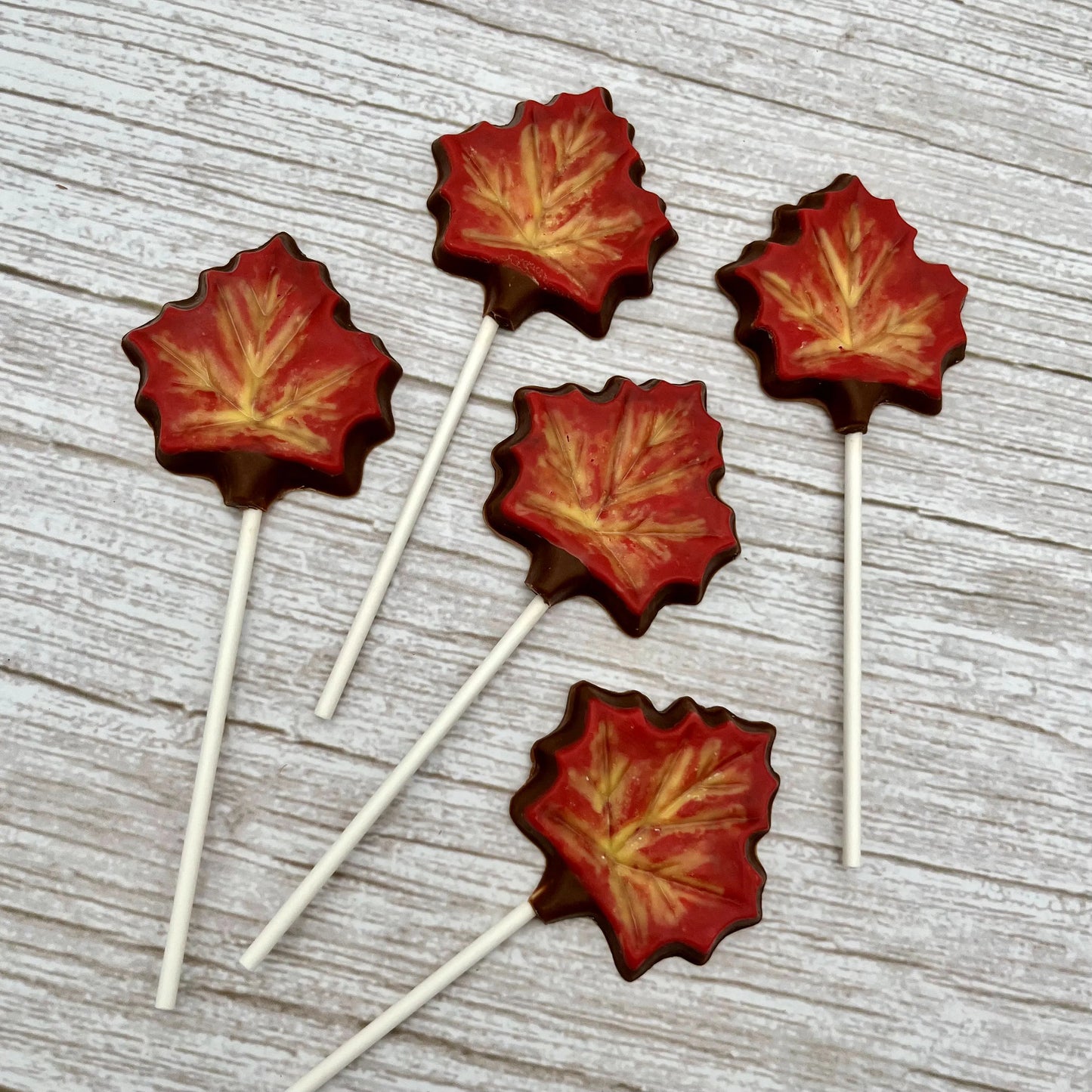 Chocolate autumn-coloured maple leaf suckers on a wooden background.