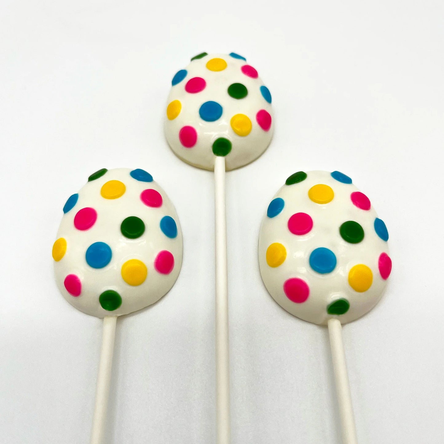 Three egg-shaped chocolate suckers, with numerous brightly coloured polka dots on a white background.