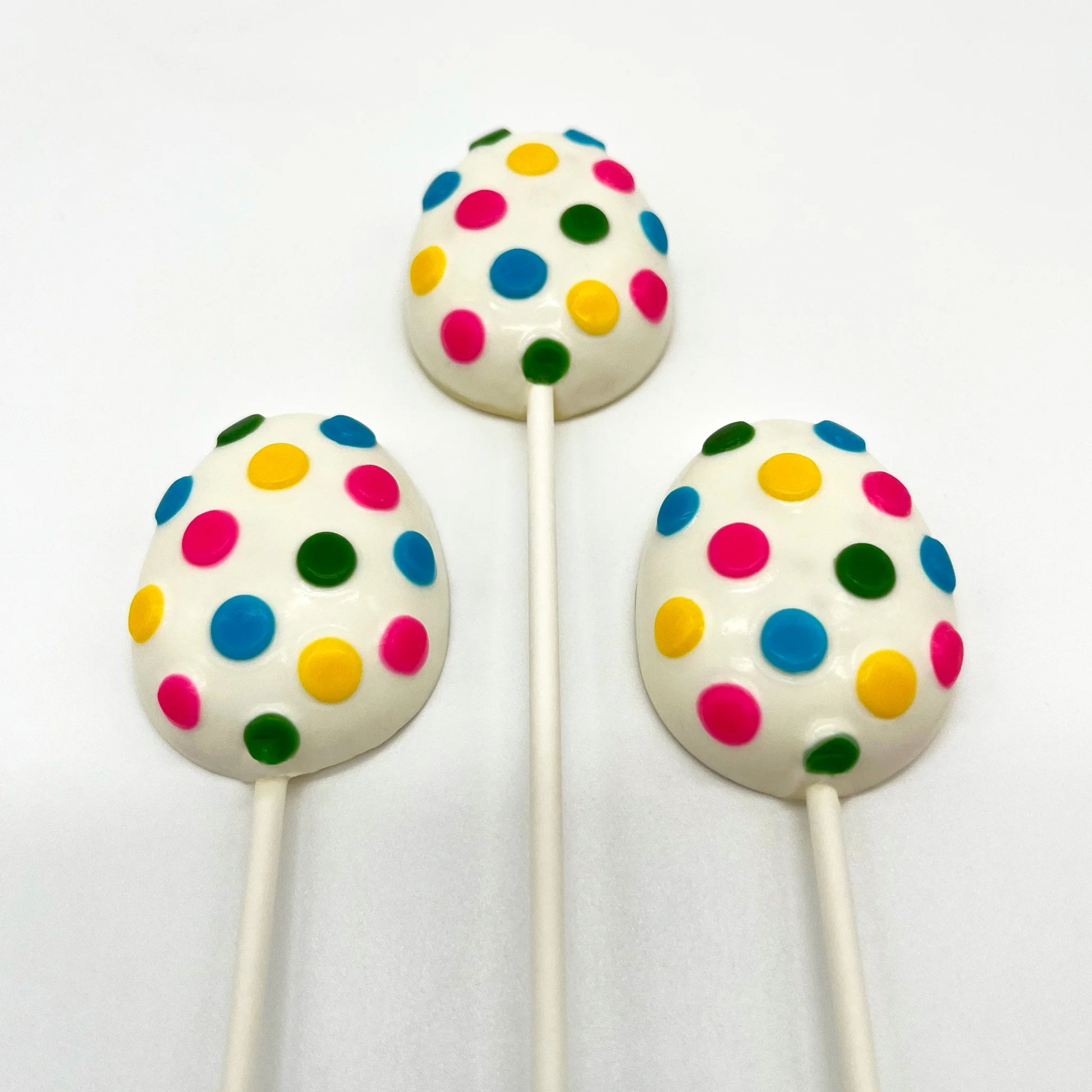Three egg-shaped chocolate suckers, with numerous brightly coloured polka dots on a white background.