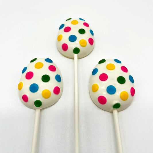 Three egg-shaped chocolate suckers, with numerous brightly coloured polka dots on a white background.