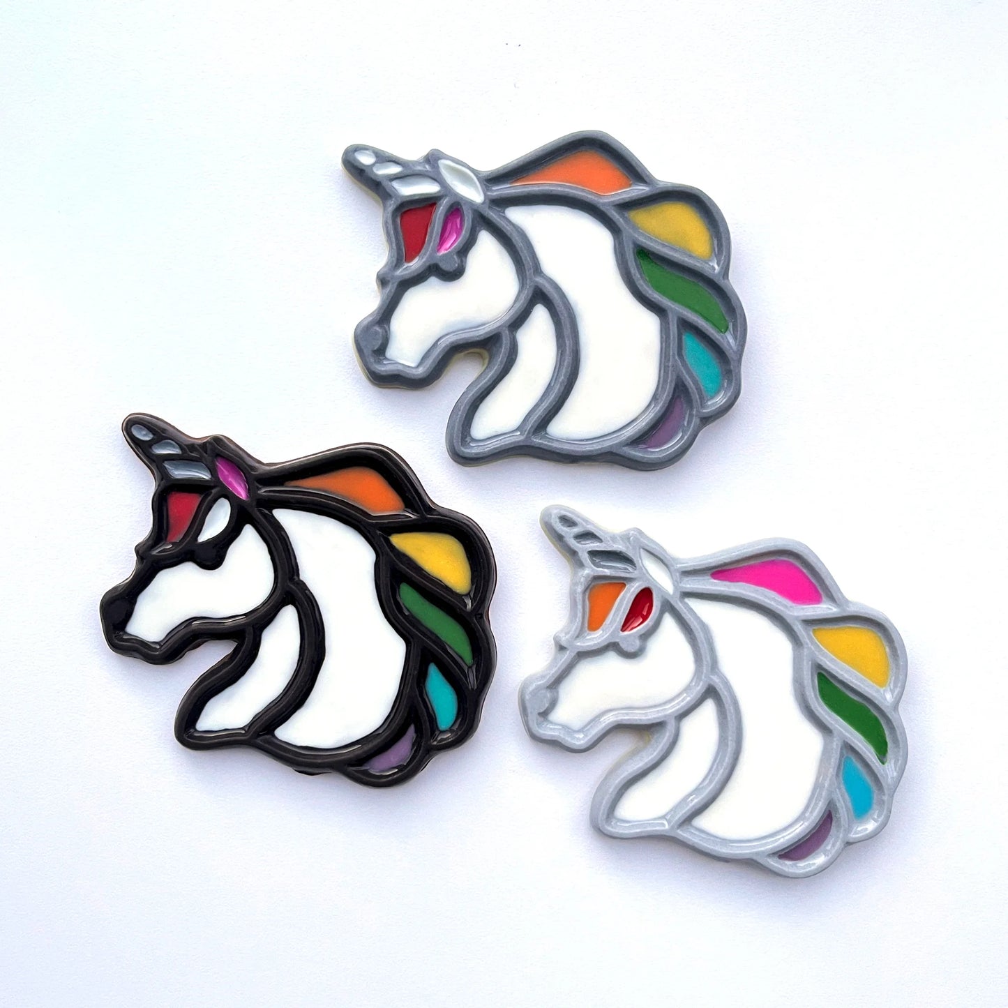 Flat, stained-glass style unicorn heads with multi-coloured rainbow manes, outlined in grey or black.