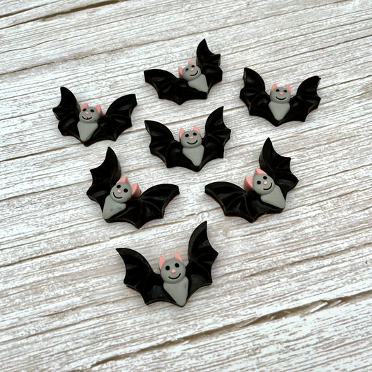 Black and grey bat-shaped chocolates with pink ears and noses and big smile. Displayed on a wooden surface.