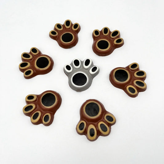 Selection of bear paw chocolates, hand-painted with black pads surrounded by white or beige, with grey or brown background.