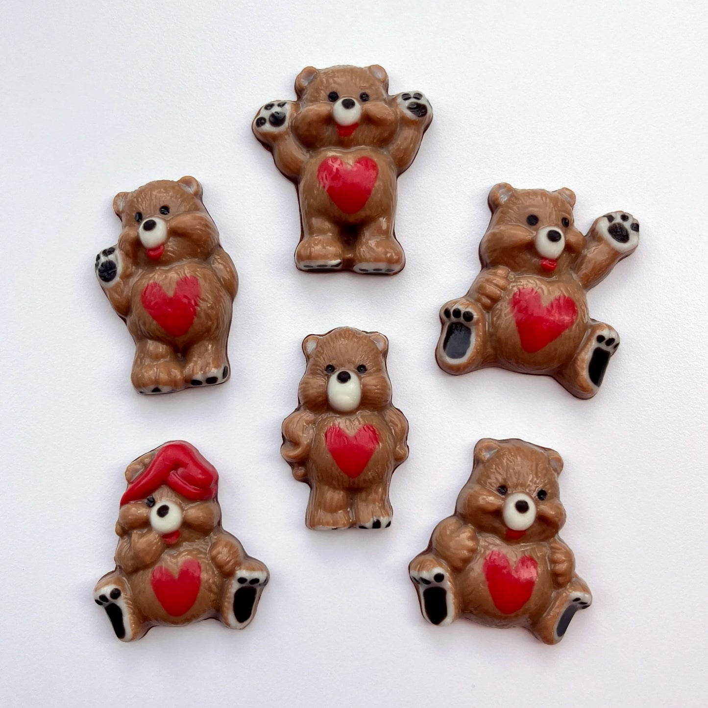Six different chocolate bears in different positions, all decorated in brown, with red hearts on their tummies and black paws. 