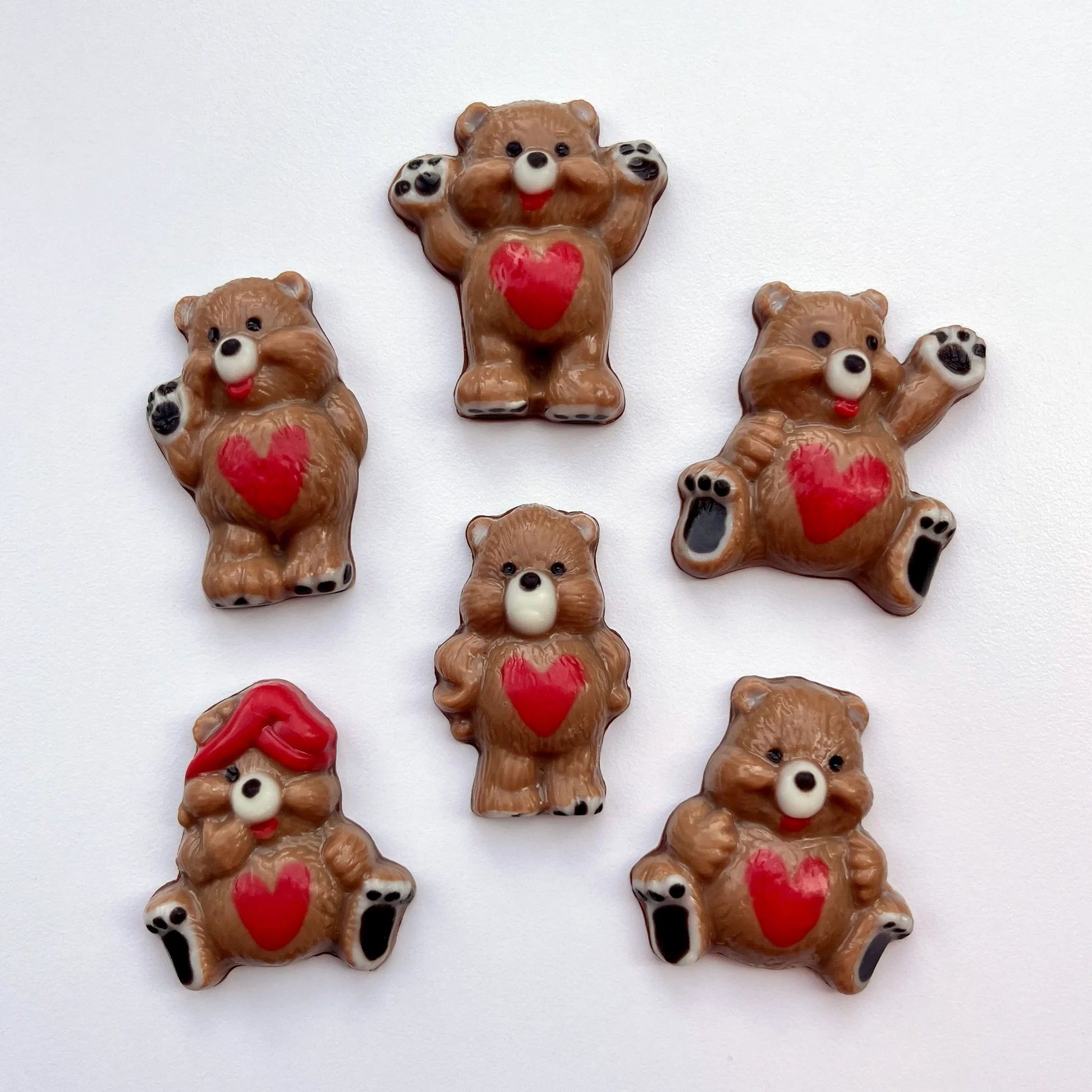 Six different chocolate bears in different positions, all decorated in brown, with red hearts on their tummies and black paws. 