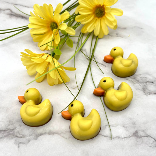 Four yellow chocolate "rubber" duckies with orange beaks on a marble surface with yellow flowers.
