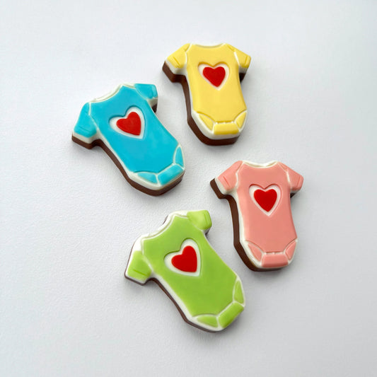 Chocolate baby onesies in four different colours - pink, blue, green and yellow, all with a red heart on the front.