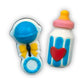 Hand-painted chocolates of blue-themed baby rattle with yellow ribbon, and milk bottle with red heart, yellow and pink top.