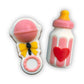Hand-painted chocolates of pink-themed baby rattle with yellow ribbon, and milk bottle with red heart, yellow and pink top.