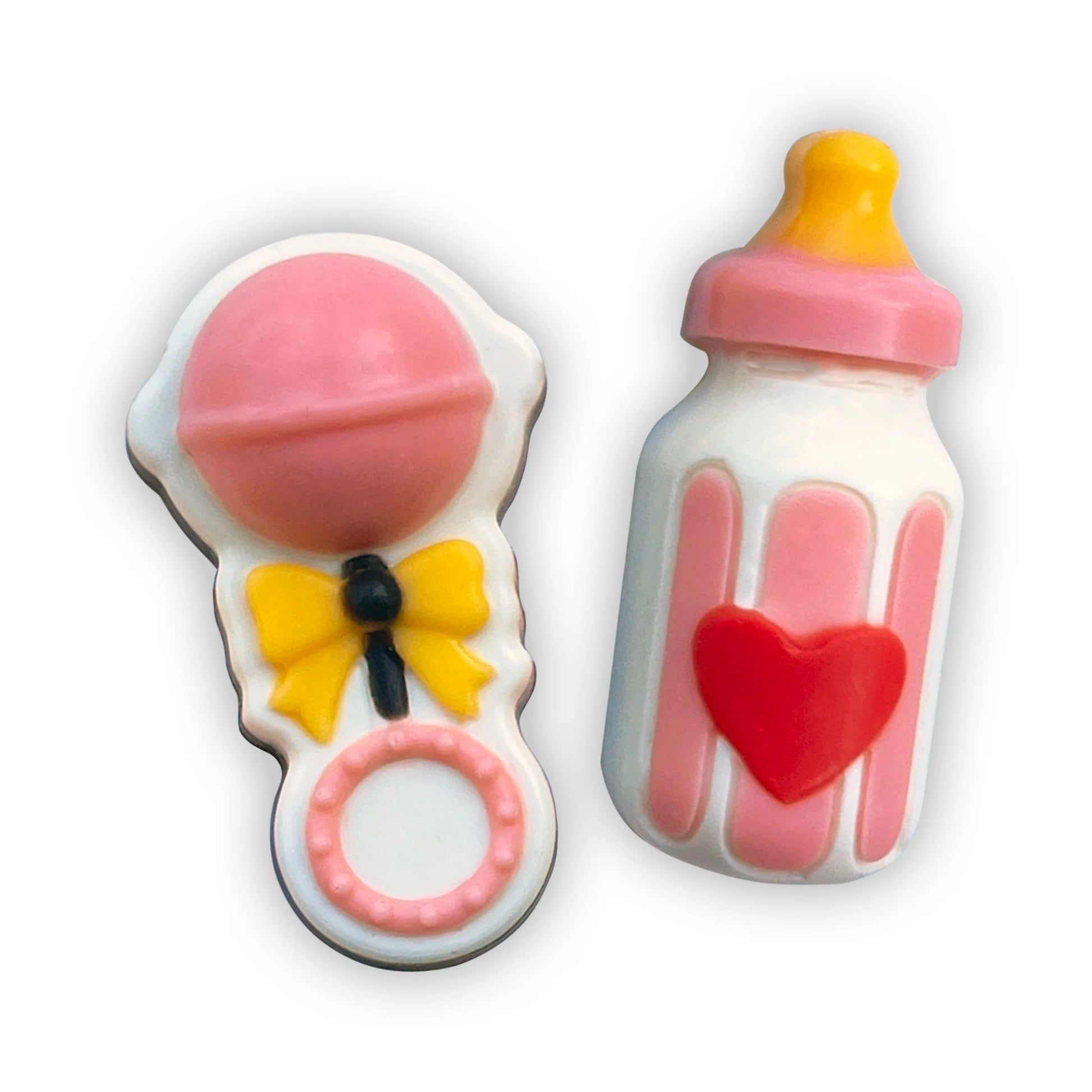 Hand-painted chocolates of pink-themed baby rattle with yellow ribbon, and milk bottle with red heart, yellow and pink top.