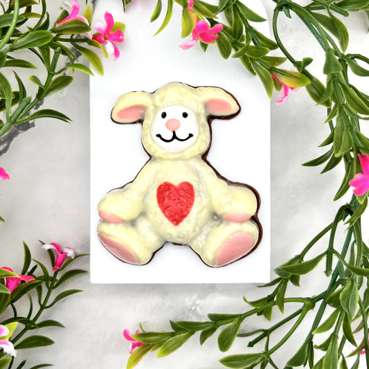 Lamb stuffie made from chocolate. Cream-coloured body with pink ears, paws and nose, white face with black eyes and smile, and a red heart on its tummy.