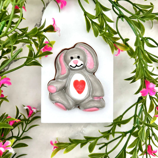 Rabbit stuffie made from chocolate. Grey body with pink ears, paws and nose, white face with black eyes and smile, and a red heart on its white tummy.