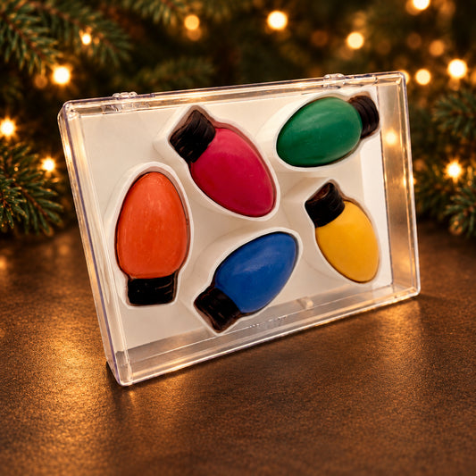 Five colourful chocolate Christmas light bulbs in a clear acrylic gift box beside glowing holiday lights.