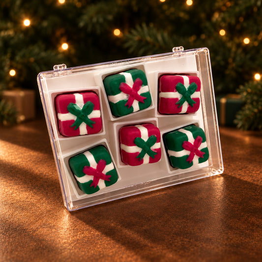 Six red and green chocolate presents with white ribbons and contrasting bows in a clear acrylic gift box.