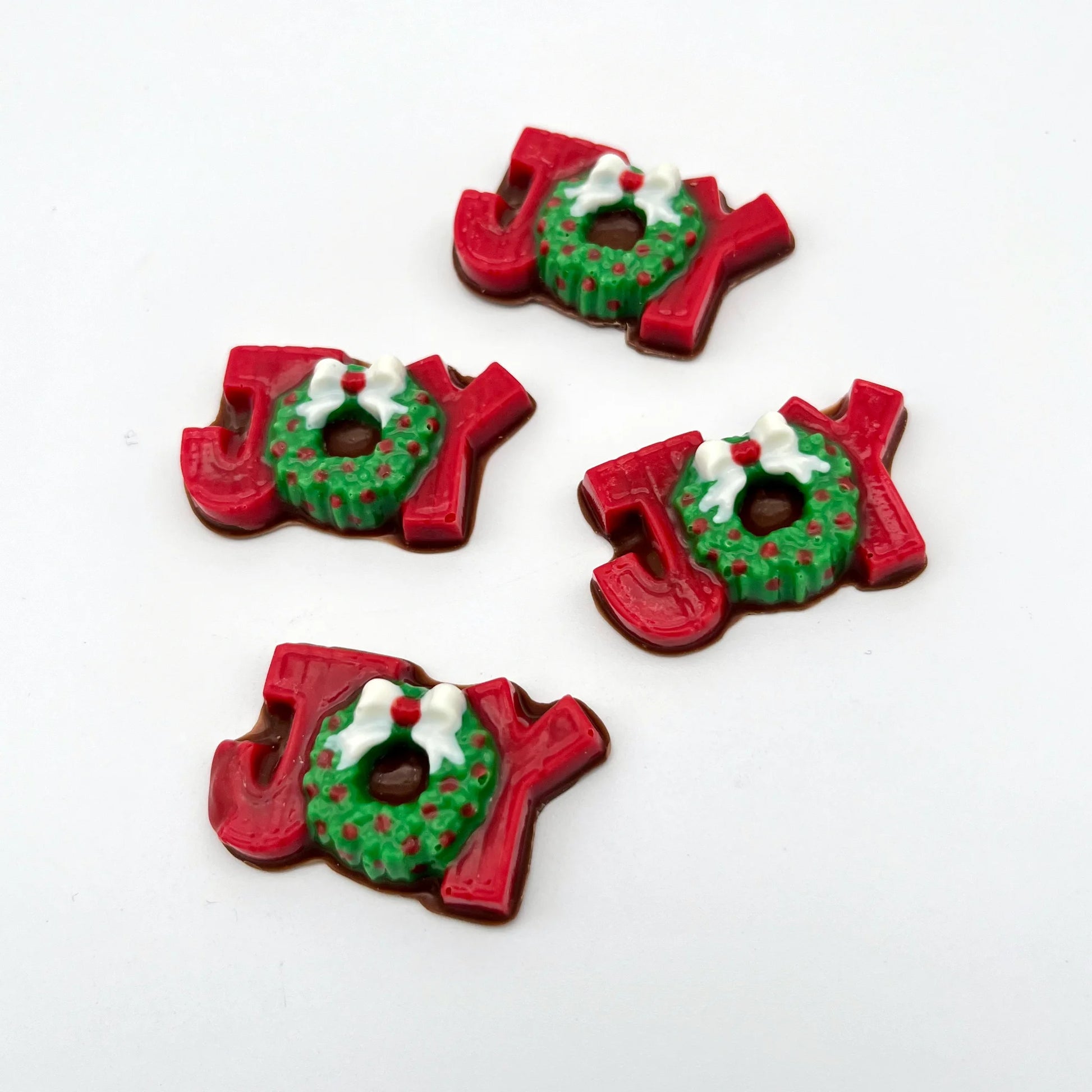 The word JOY made from chocolate. The J and Y are red, and the O is a green wreath with red berries and a white bow.