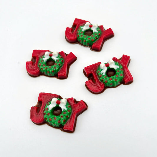 The word JOY made from chocolate. The J and Y are red, and the O is a green wreath with red berries and a white bow.