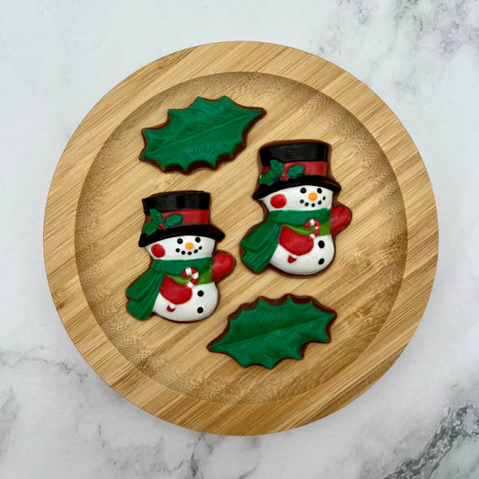 Two festive chocolate snowmen with top hats, green scarves, and red mittens holding a candy cane.
