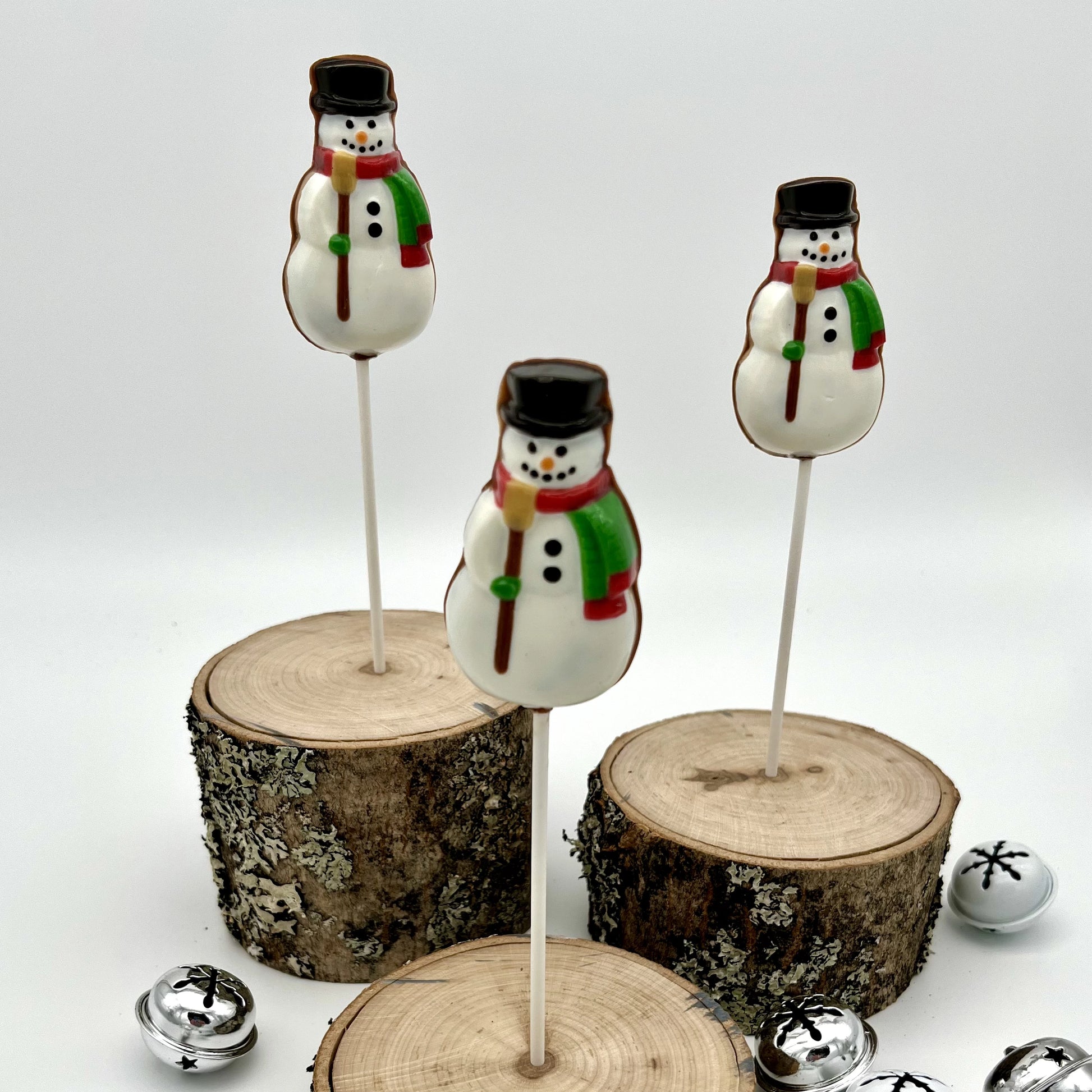Classic white snowmen suckers made of chocolate, adorned with a broom, red and green scarf, and a black hat.