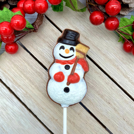 Cheery chocolate snowman sucker with red scarf and mittens, black top hat, holding a broom, surrounded by festive berries.