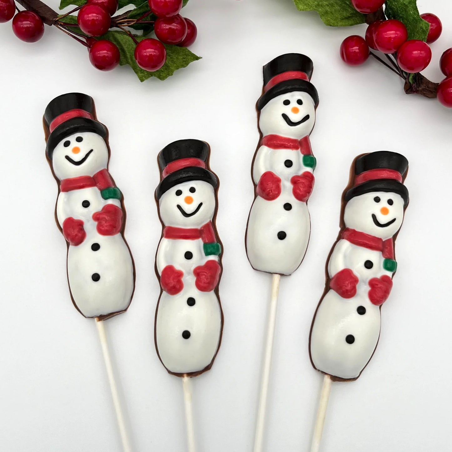 Three chocolate suckers of tall snowmen, adorned with red mittens and scarves, and a black top hat with red band.