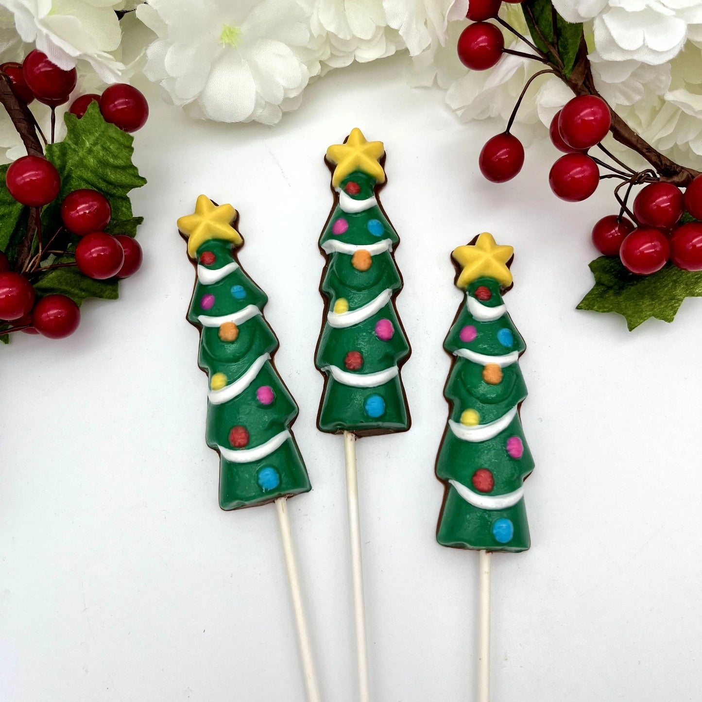Three chocolate suckers shaped like Christmas trees with colourful decorations and a yellow star on top.