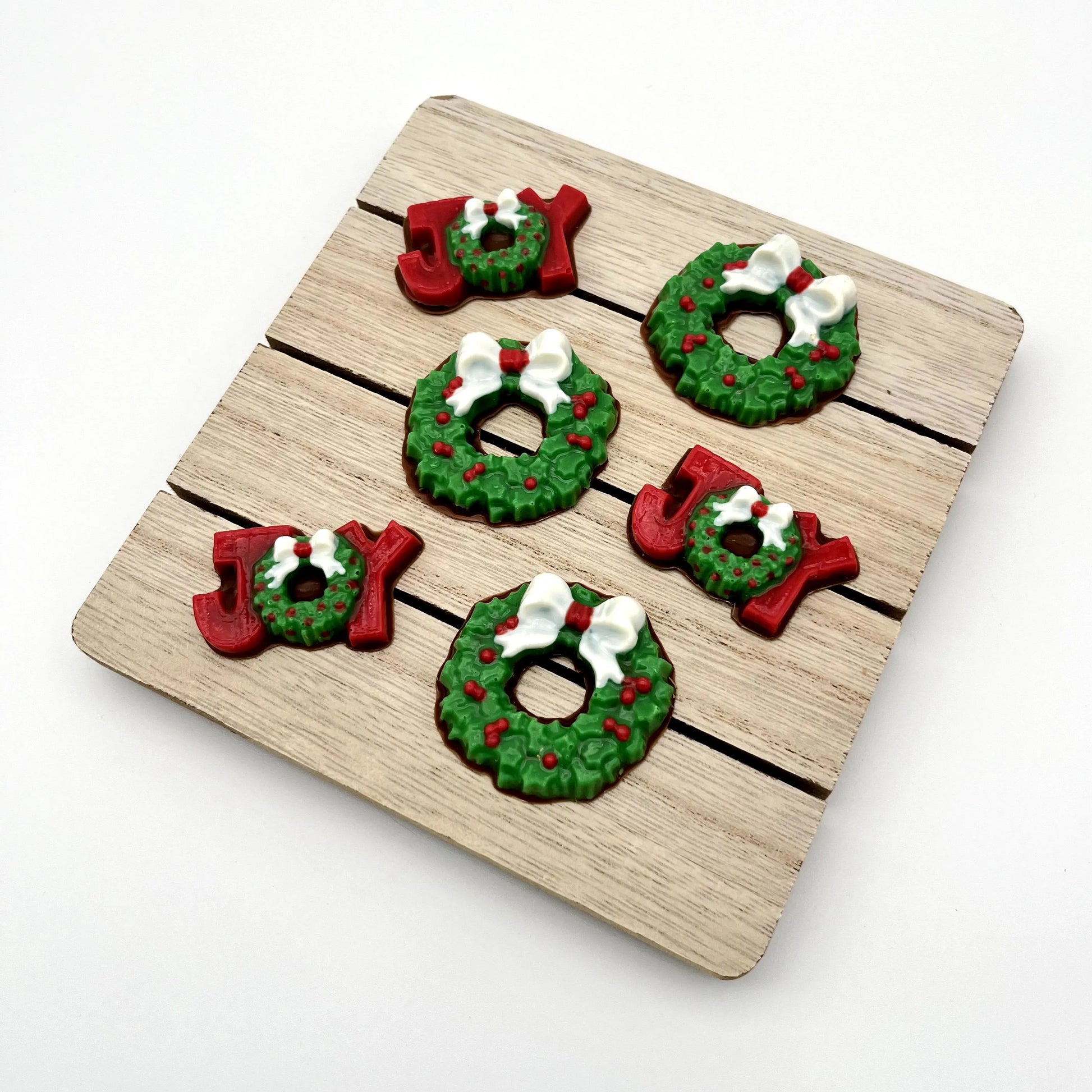 Chocolate Christmas wreaths, plus the word JOY; the J and Y are red, and the O is a wreath. All coloured in traditional green with red berries and white bow.